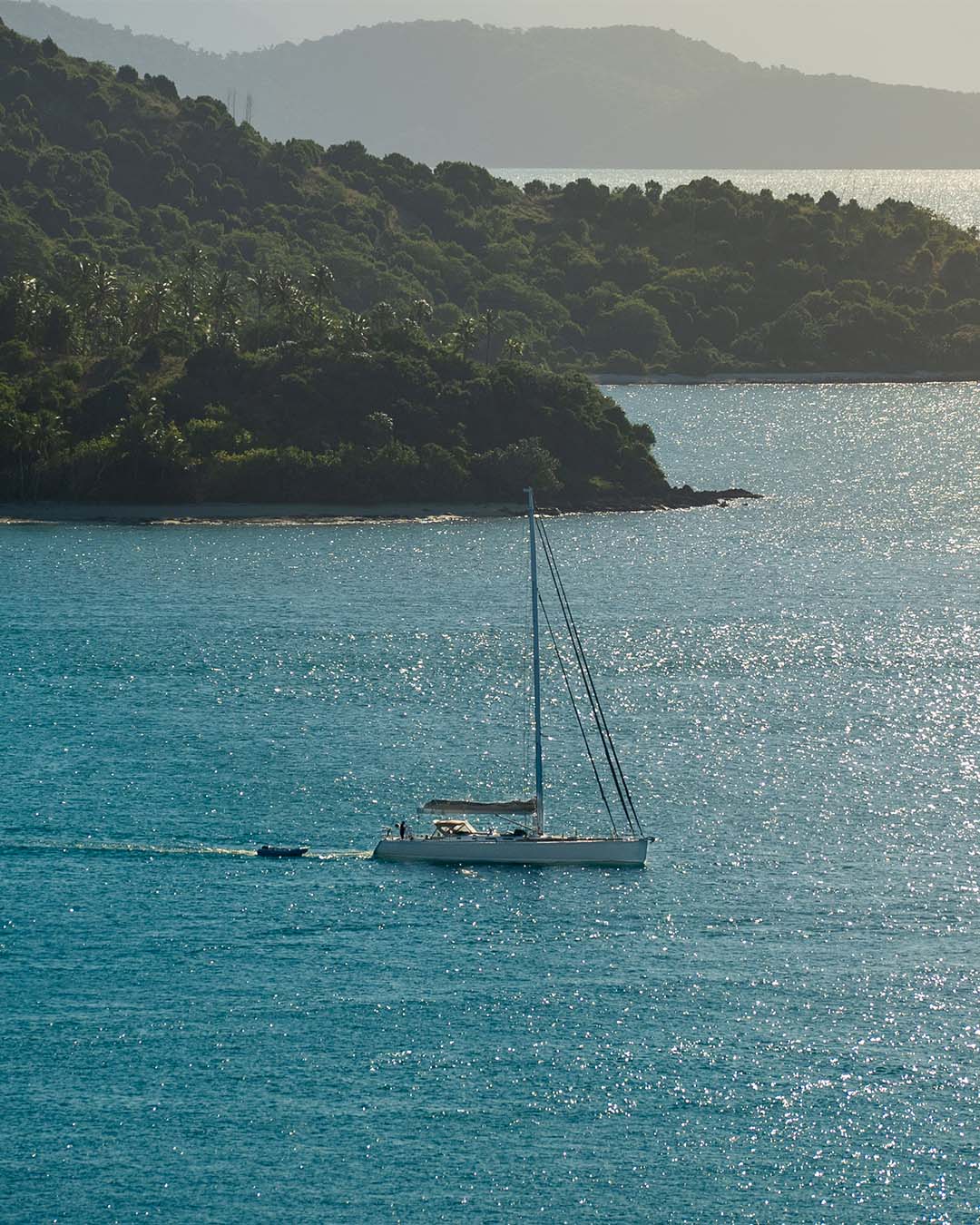 Sailboat on a clear blue sea with a lush Hamilton island in the background