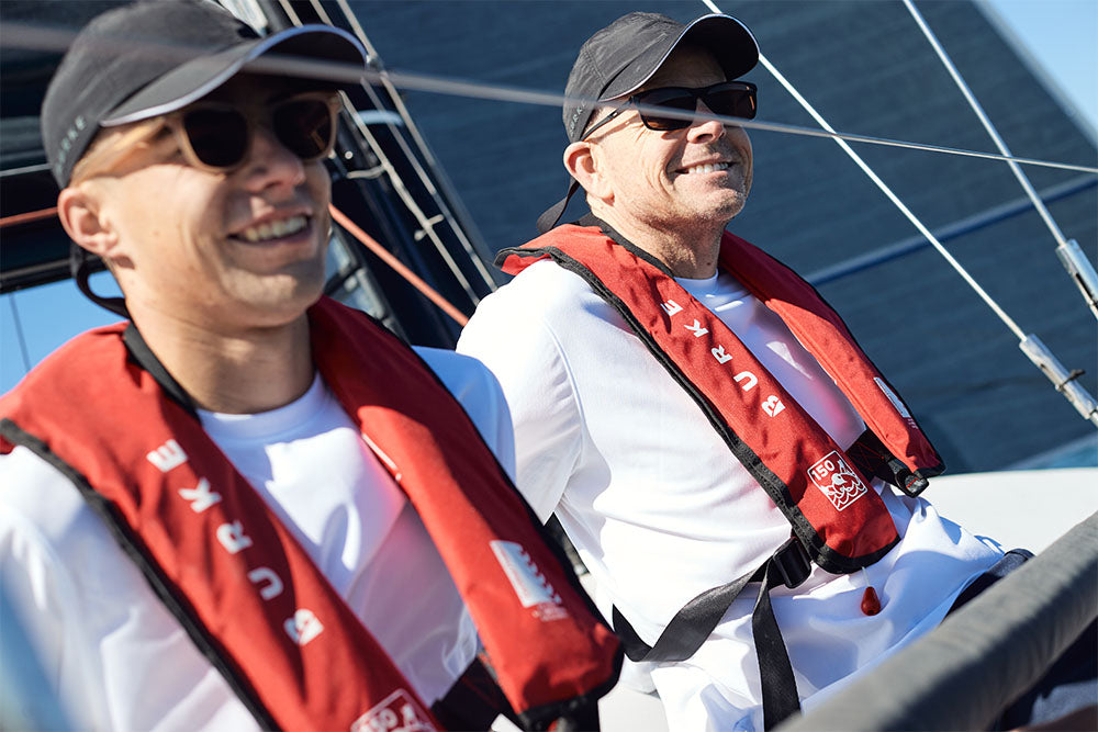 Two men sailing, wearing Burke Standard Inflatable PFD - Level 150 - Red and White Burke Crew Technical Tees